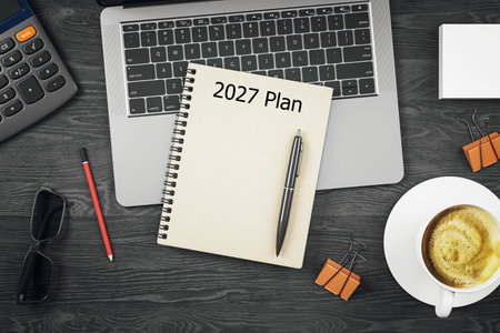 Top view of a planner notebook labeled 2027 Plan with pen on dark desk background, surrounded by...