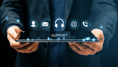 Businessman holding tablet with digital support icons on dark background, symbolizing online help,...