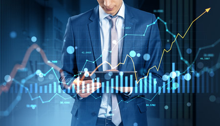 Businessman in suit using tablet with financial graphs, charts, and currency data overlay on modern...