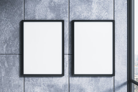 Two vertical blank posters in black frames on a stone concrete wall, closeup indoors with window...