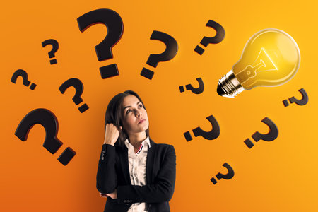 Businesswoman thinking with question marks and glowing lightbulb above her on bright orange background, concept of idea, problem, and creativityの写真素材