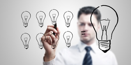 Young business man drawing many small light bulbs equal a big one.の写真素材