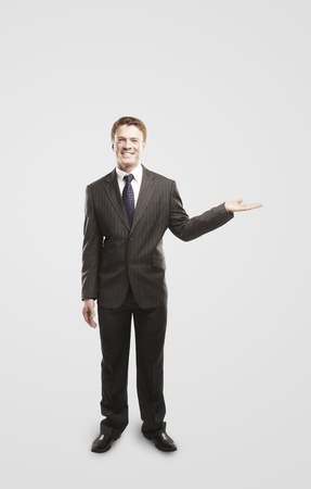 Smiling young  businessman presenting something on empty hand. On a gray backgroundの写真素材