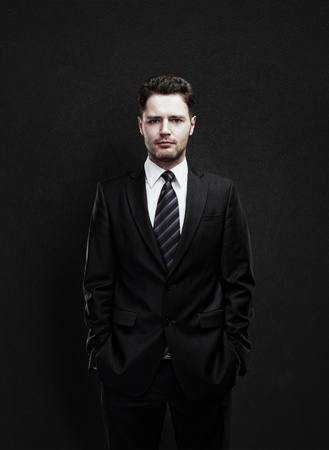Portrait of a young businessman standing with his hands in the pockets  Young handsome man  looking confident  On a black  backgroundの写真素材