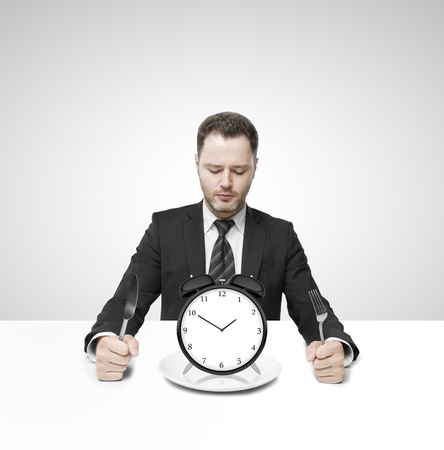 businessman sitting on table and eating clockの写真素材