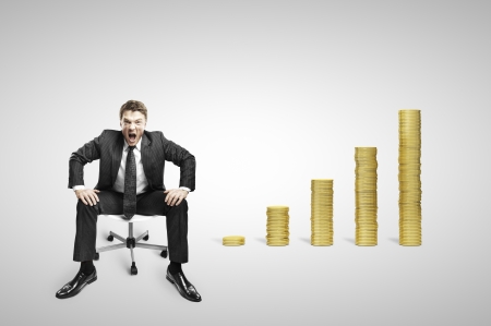businessman sitting on chair and screaming with coins stacksの写真素材