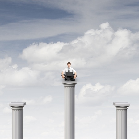 businessman sitting on column with notebook on a sky backgroundの写真素材