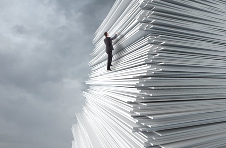 businessman climbing up a huge stack of paperの写真素材