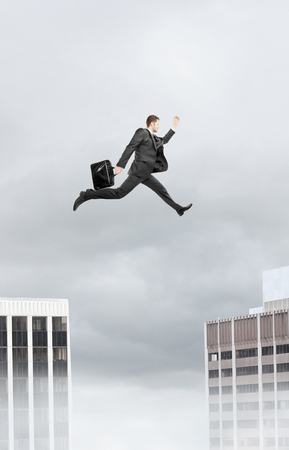businessman jumping from roof to roof on cityの写真素材