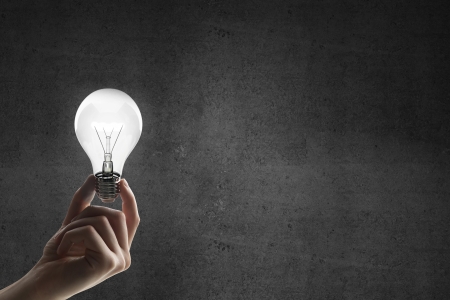 hand holding lightbulb on a concrete backgroundの写真素材