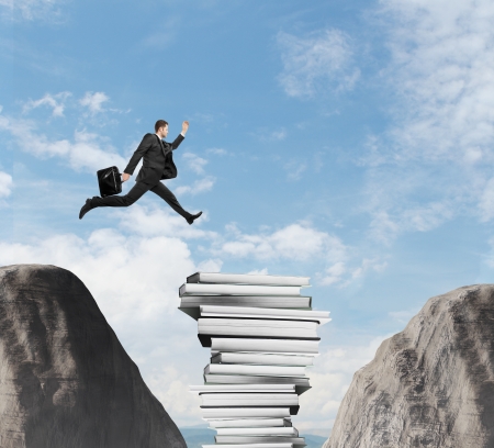 Businessman jumping from a rock through booksの写真素材