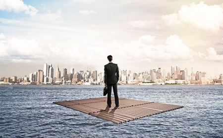 businessman standing on raft and looking to cityの写真素材