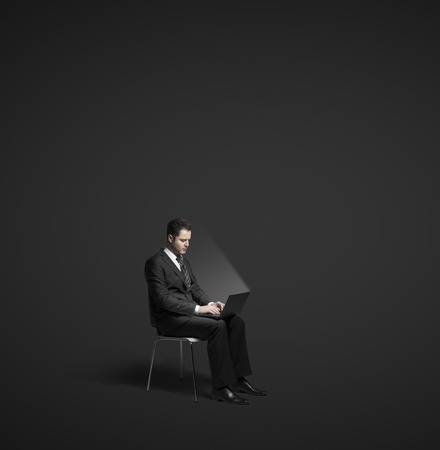 businessman sitting with laptop on black backgroundの写真素材