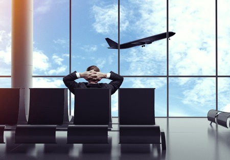 businessman sitting in airport  and looking to airplane in skyの写真素材