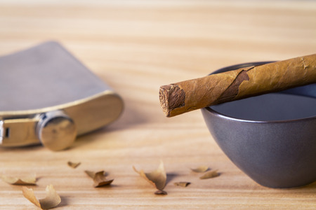 Closeup of desktop with cigar on top of coffee cup, silver flask and filing on concrete backgroundの写真素材