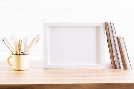 Wooden desktop with blank picture frame, pencils in iron mug and books. Mock upの写真素材