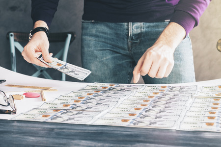 Businessman sorting out dollar banknote rows on wooden tableの写真素材