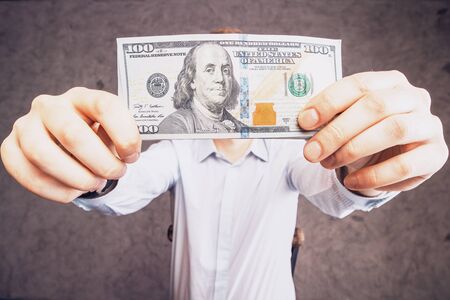 Male holding one hundred dollar bill on concrete backgroundの写真素材