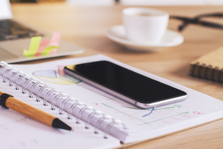 Closeup of wooden workspace with phone on business chartの写真素材