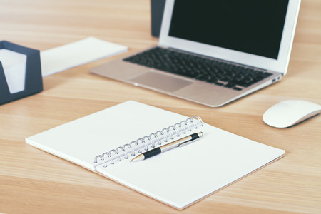 Table with blank blurry laptop screen and notebookの写真素材
