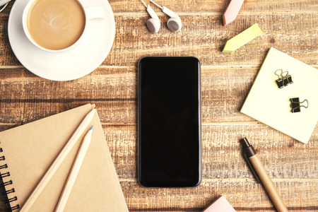 Top view of wooden table with blank phone, coffee and office tools.の写真素材