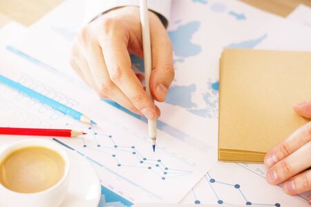 Closeup of male hand with pencil analyzing business report with charts and graphsの写真素材