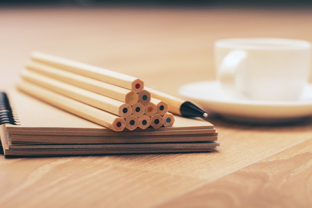 Wooden desktop with colorful pencil pyramid on notepad and coffee cupの写真素材