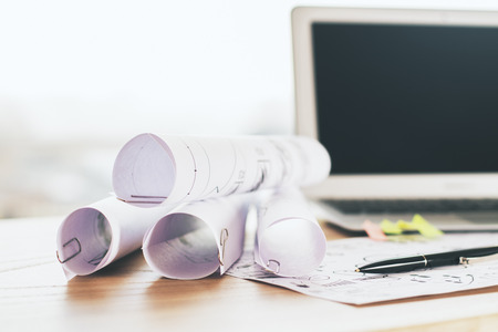 Closeup of rolled paper sheets on wooden desktop with blurry laptop screen in the background