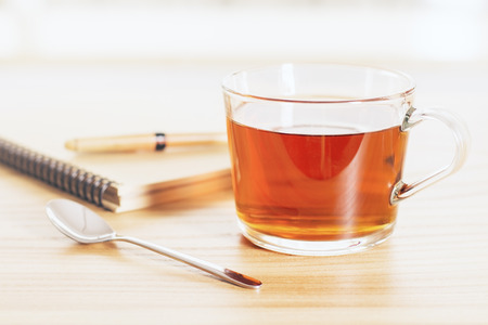 Cup of tea on wooden table with teaspoon and spiral copybookの写真素材