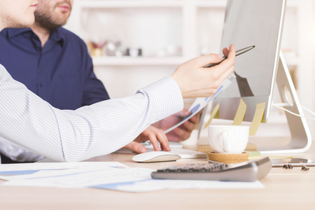 Sideview of businessmen discussing business charts and pointing at computer screen in officeの写真素材