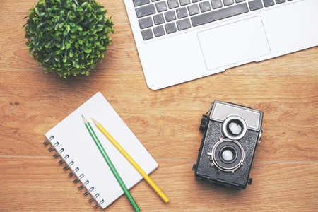 Topview of desktop with plant, laptop keyboard, notepad with pencils and retro camera