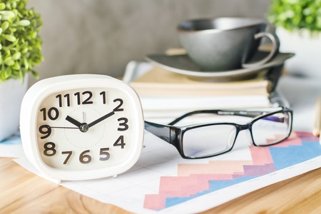 Closeup of white clock on wooden table with plants, glasses and coffee cupの写真素材