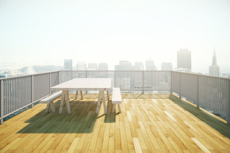 Balcony design with table and benches, wooden floor and railing on sunlit city background. 3D Renderingの写真素材