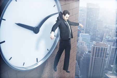 Time management concept with businessman hanging on clock arrow above city. 3D Renderingの写真素材