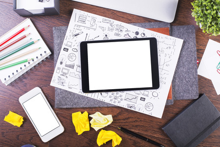 Top view of creative dark wooden desktop with blank white tablet, business sketch, smartphone and various office tools. Mock upの写真素材