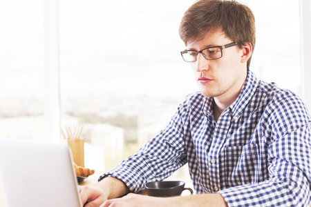 Handsome caucasian man using laptop on table with coffee, croissant and pencils pn blurry background