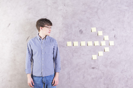 Caucasian male looking at sticker arrow glued onto concrete wall