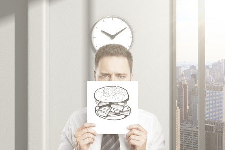 Frowny businessman can't wait for lunch break, holding hamburger sketch in office interior with clock and city view. 3D Renderingの写真素材