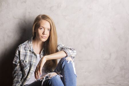 Attractive young woman sitting against concrete wallの写真素材