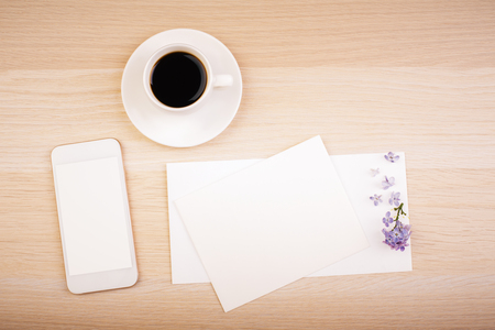 Top view of wooden desktop with blank whte smart phone screen, empty card and coffee cup. Mock upの写真素材