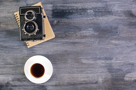 Top view of dark wooden desktop with coffee cup, retro camera and notepad. Mock upの写真素材