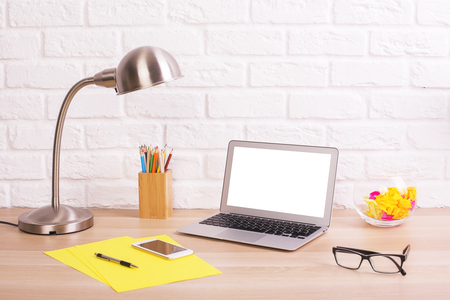 Creative office desktop with blank white laptop screen, lamp,glasses, smart phone, yellow paper sheets and other items. Mock upの写真素材