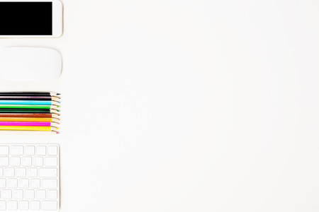Top view of white desktop with keybopard, blank phone, computer mouse and colorful pencils. Mock up