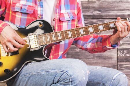 Closeup of electric guitar in casual guy's hands on wooden backgroundの写真素材