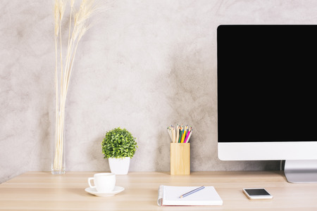 Closeup of creative designer desktop with blank computer monitor, coffee cup, smart phone and other items on concrete background. Mock upの写真素材