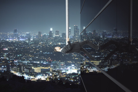 Success concept with businessman holding onto rope and climbing building on illuminated night city backgroundの写真素材