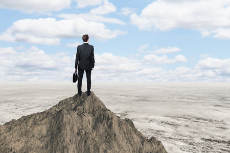 Research concept with businessman standing on mountain top and looking at desertの写真素材