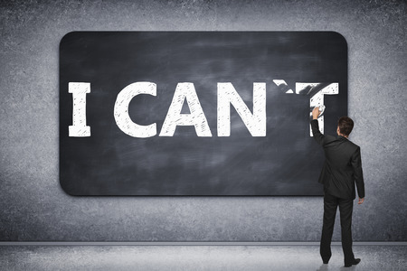 I can, self motivation concept. Businessman wiping letter 'T off chalkboard in concrete room so that it reads i canの写真素材