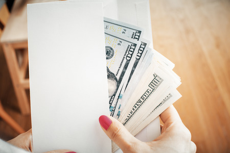 Corruption and bribery concept with female hands holding envelope with dollar banknotes on wooden background. Mock upの写真素材