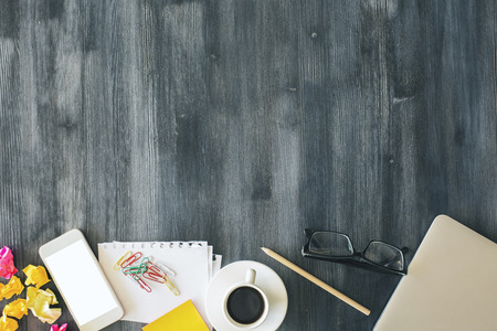 Top view of messy office desktop with crumpled paper, blank white smartphone, coffee cup, glasses and other items. Mock upの写真素材